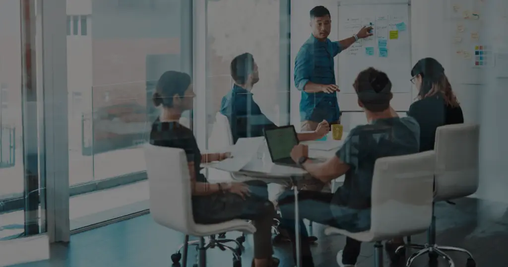 Business meeting in brightly lit room with presenter pointing to a line chart.
